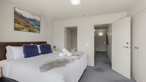 A bedroom with a large bed, a painting on the wall, and a hallway leading to another room. - Alpine Village 23 - 2 bed with lake views (Queenstown)