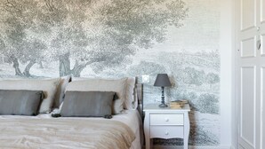 A bedroom with a bed, pillows, a nightstand with a lamp, and a wall with a tree mural. - ÔVILLAGE  (Ouveillan)