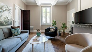 A living room with a sofa, armchair, coffee table, and a TV mounted on the wall. - ÔVILLAGE  (Ouveillan)