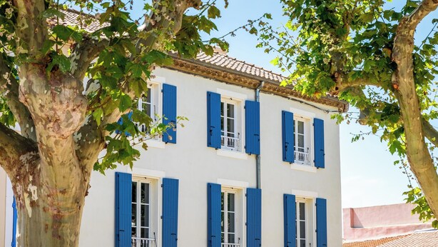 A white building with blue shutters and a tiled roof. - ÔVILLAGE  (Ouveillan)