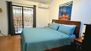 Een slaapkamer met een bed, een schilderij, een raam met gordijnen en een betegelde vloer.