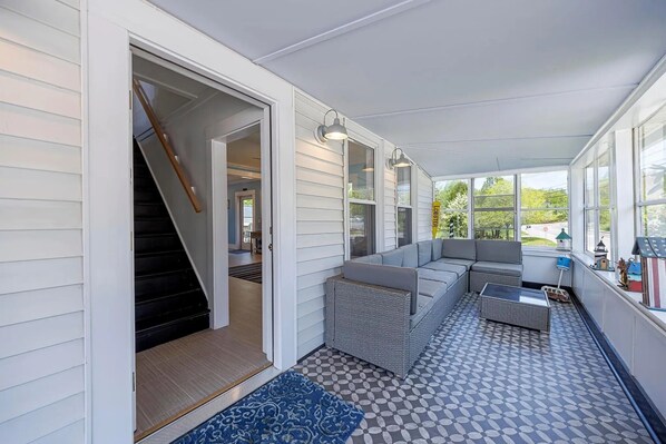A covered porch with a sofa, a small table, and a patterned floor. - Former Lighthouse Keeper's Home - Southwest Harbor Village. Highspeed Wi-Fi & AC (Southwest Harbor)