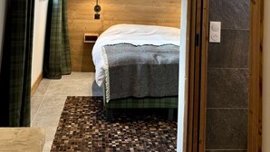 A bedroom with a bed, a nightstand, a lamp, a window with curtains, and a door.