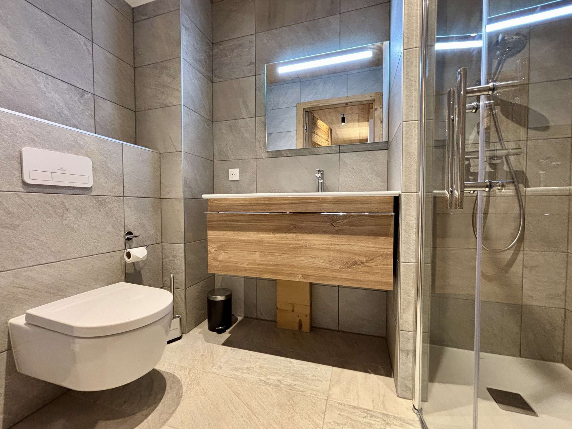 A modern bathroom with a toilet, sink, mirror, and shower.