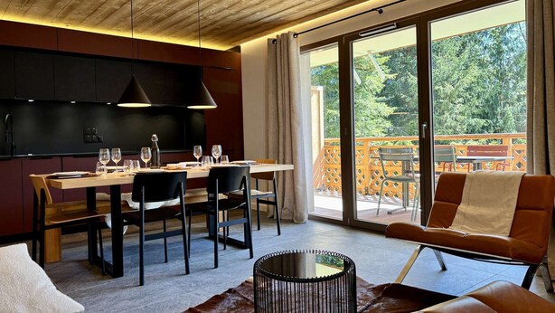 A modern dining area with a wooden ceiling, a large sliding glass door leading to a balcony, and a cozy seating area with leather furniture.