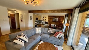 A modern living room with a grey sectional sofa, a wooden coffee table, and a kitchen in the background. - Large, bright T4 in the heart of Châtel (CHATEL)