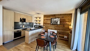 A modern kitchen with wooden cabinets, a central island, and a dining area with a table set for four. - Large, bright T4 in the heart of Châtel (CHATEL)