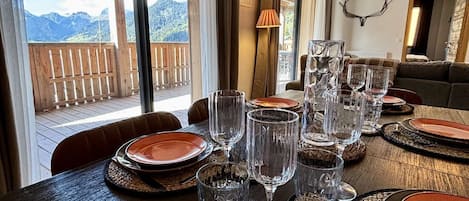 A dining area with a table set for a meal, large windows offering a mountain view, and a wooden ceiling.