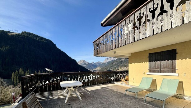 A balcony with a view of mountains, a wooden bench, and two lounge chairs.