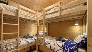 A wooden bunk bed room with a ladder, a small table, and a hanging light fixture.
