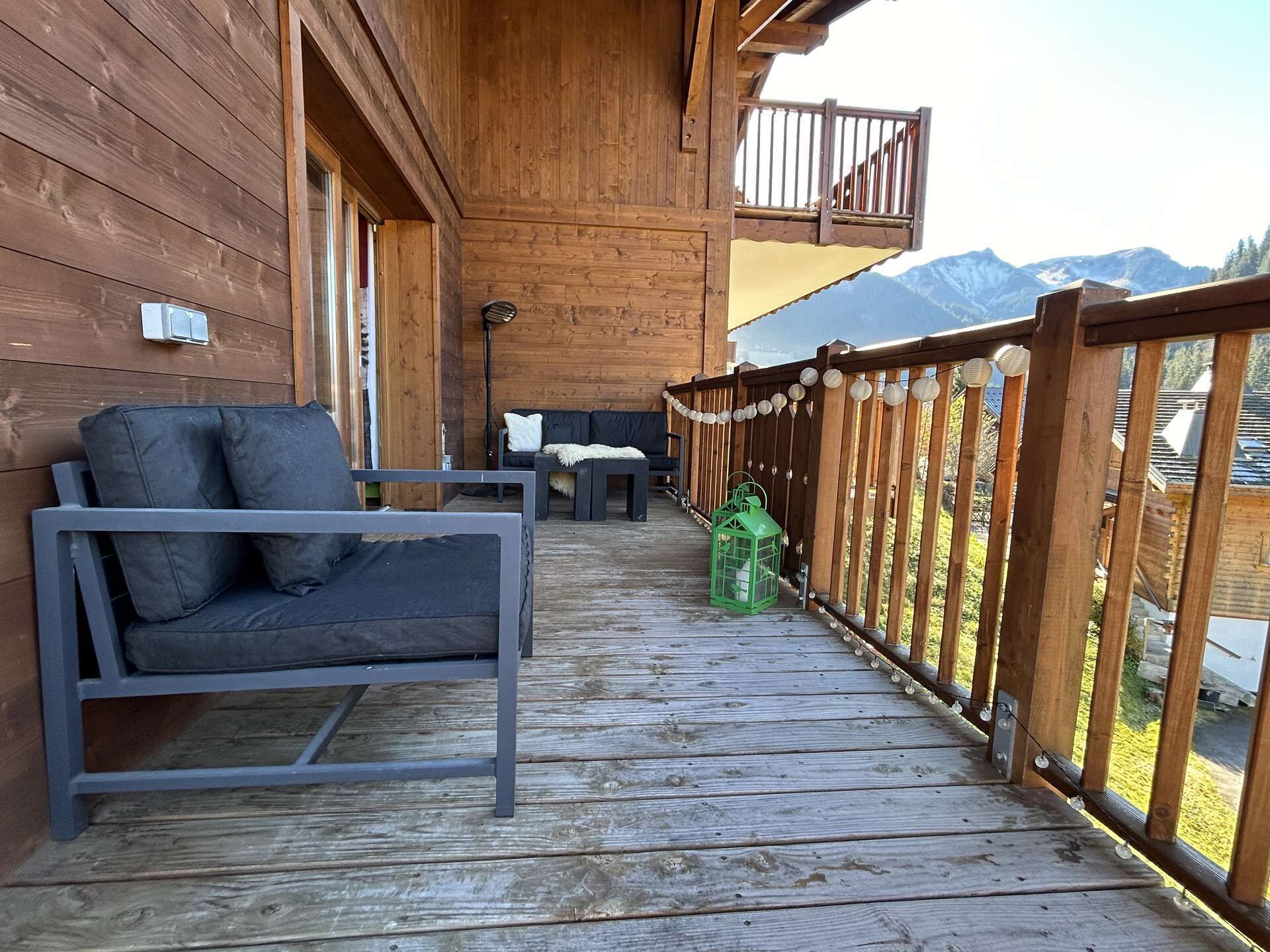 A wooden deck with a sofa and a table, overlooking a mountainous landscape.