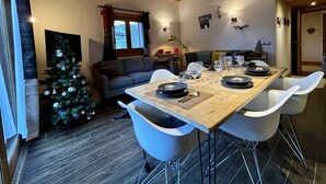 Ein moderner Essbereich mit einem Holztisch, gedeckt für vier Personen, weißen Stühlen und einem Weihnachtsbaum im Hintergrund.