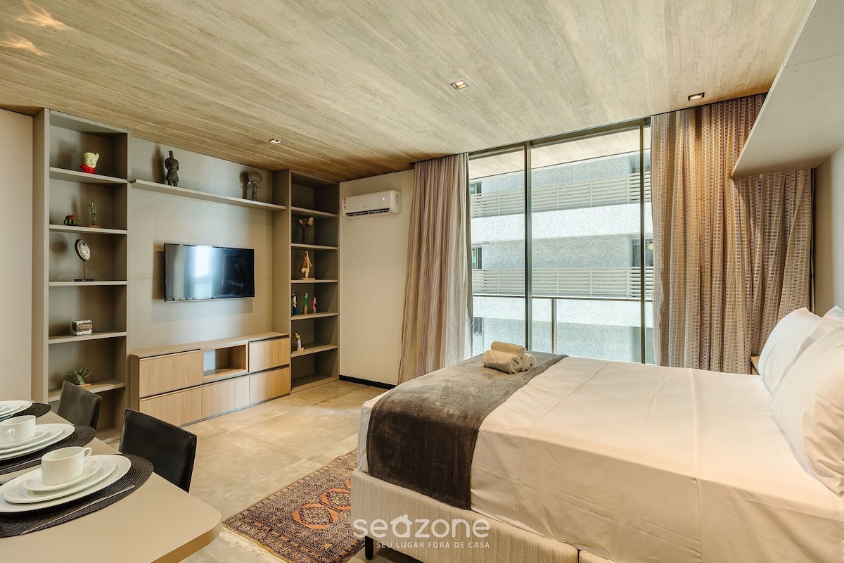 Une chambre d’hôtel moderne équipée d’un lit, d’une télévision, d’un coin repas et d’une grande fenêtre avec des rideaux.