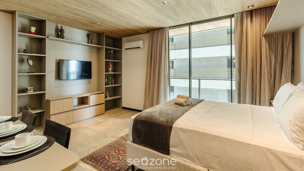 Ein modernes Hotelzimmer mit Bett, Fernseher, Essbereich und großem Fenster mit Vorhängen.