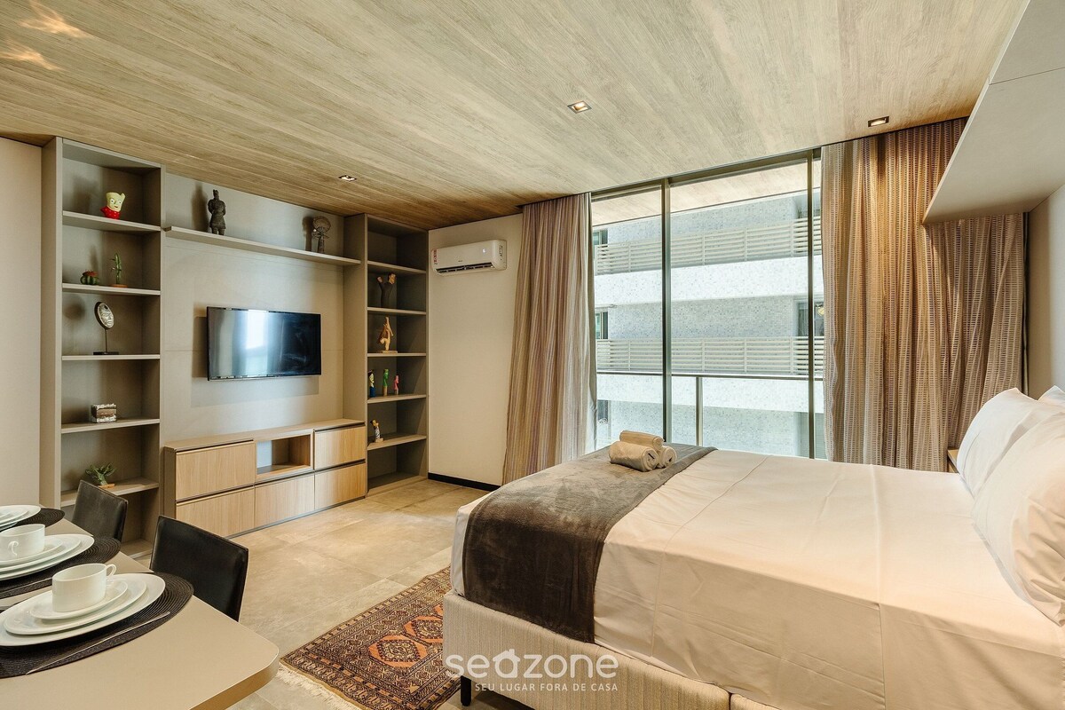 Ein modernes Hotelzimmer mit Bett, Fernseher, Essbereich und großem Fenster mit Vorhängen.