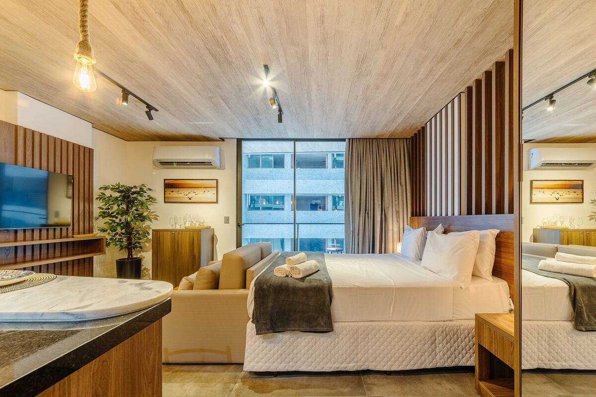 Une chambre d’hôtel moderne avec un grand lit, un canapé, une télévision et un coin repas agrémenté d’une plante.