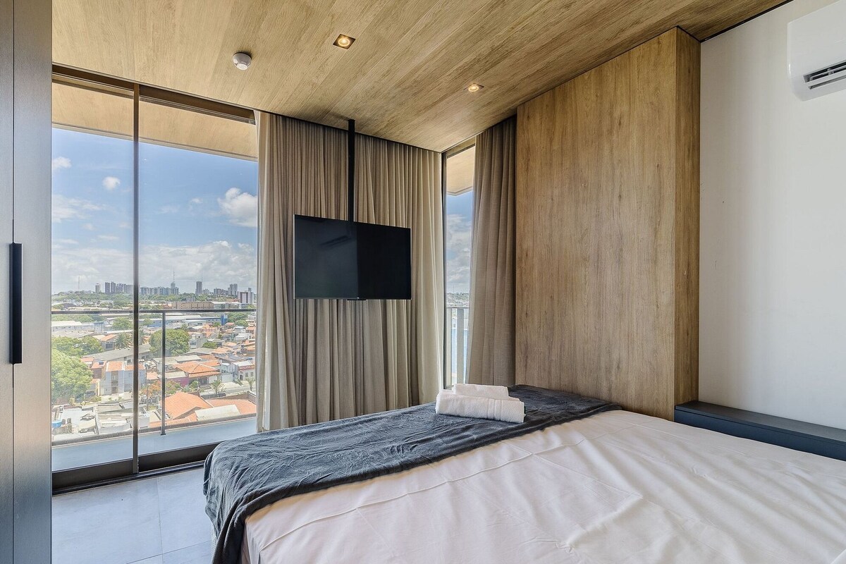 Ein modernes Hotelzimmer mit einem großen Bett, einem flachbildfernseher an der Wand und Blick auf die Stadt durch raumhohe Fenster.