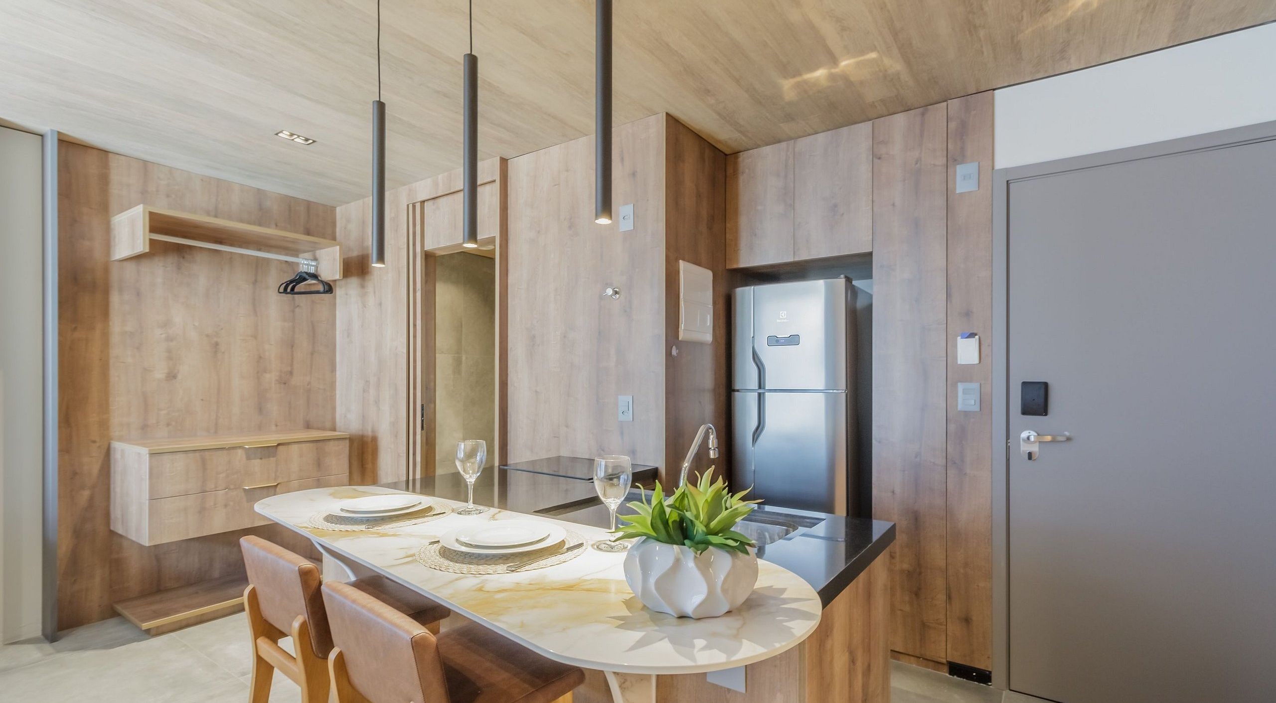 A modern kitchen with a central island, wooden cabinetry, and a stainless steel refrigerator.