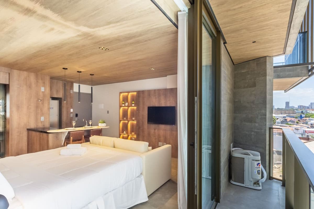 Une chambre d’hôtel moderne dotée d’un grand lit, d’un canapé, d’un petit coin cuisine et d’un balcon offrant une vue sur la ville.
