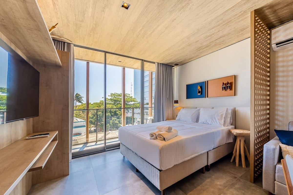 Une chambre d’hôtel moderne dotée d’un grand lit, d’une télévision, d’un balcon offrant une vue sur la ville et d’un plafond en bois.