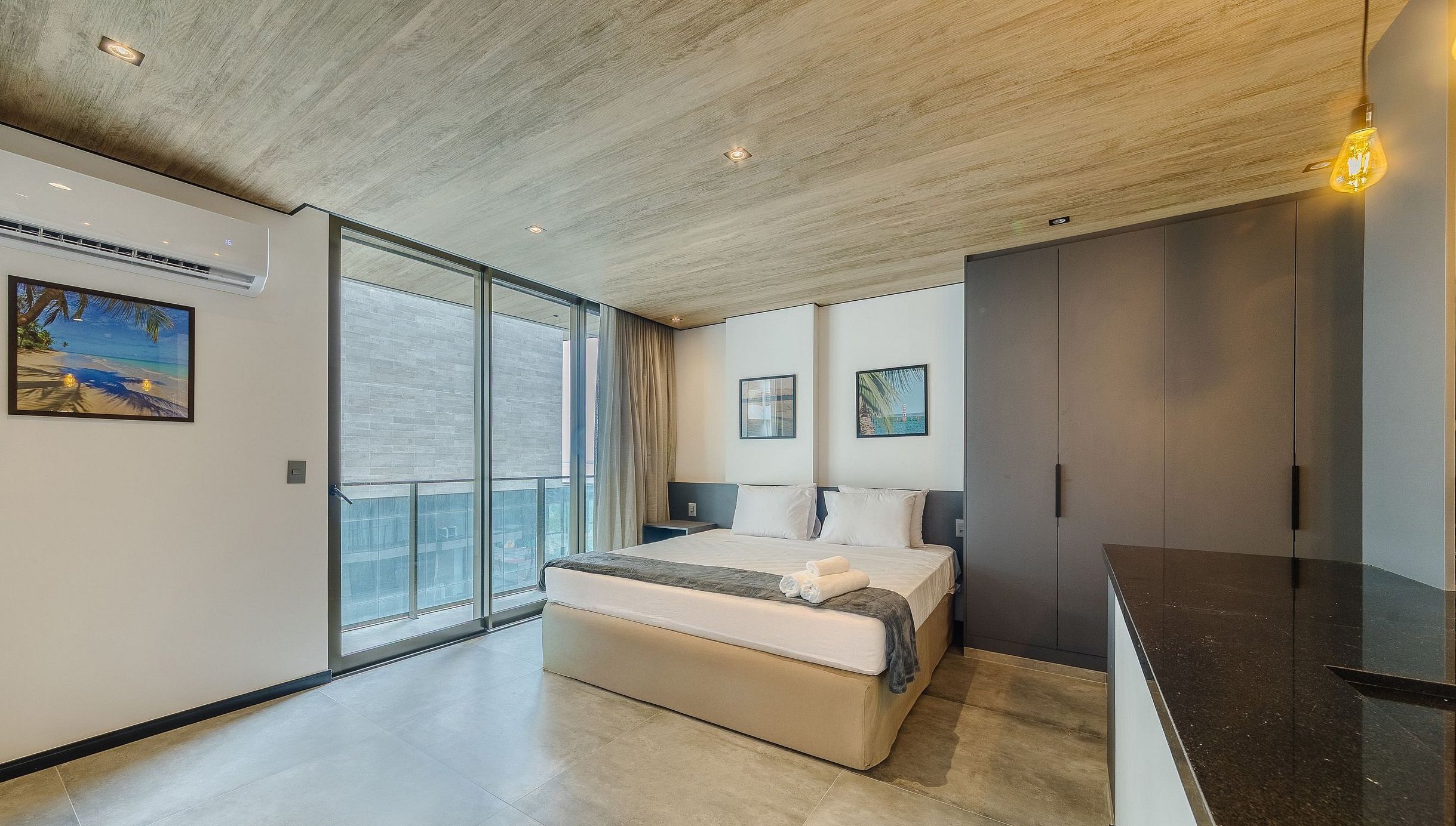 Un dormitorio moderno con una cama grande, una puerta corrediza de vidrio a un balcón y vistas de la ciudad.
