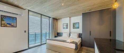 Un dormitorio moderno con una cama grande, una puerta corrediza de vidrio a un balcón y vistas de la ciudad.