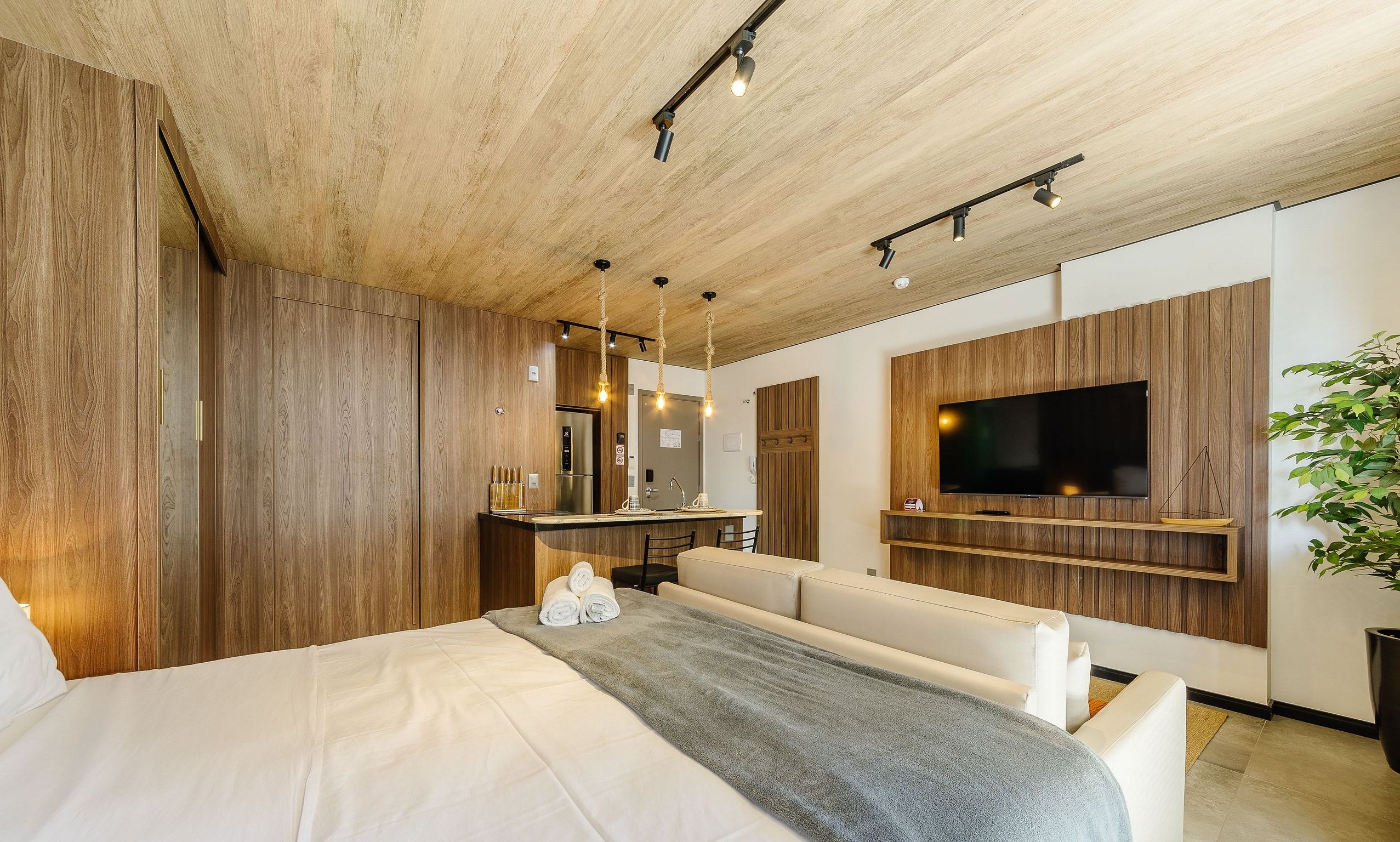 Une chambre d’hôtel moderne avec un plafond en bois, un grand lit, un coin salon, une télévision et une petite kitchenette.