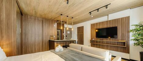 Une chambre d’hôtel moderne avec un plafond en bois, un grand lit, un coin salon, une télévision et une petite kitchenette.