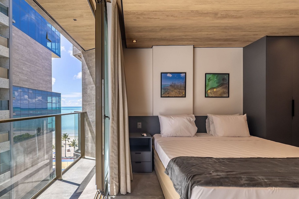 Un dormitorio moderno con una cama grande, una mesita de noche, un armario y un balcón con vista al mar.
