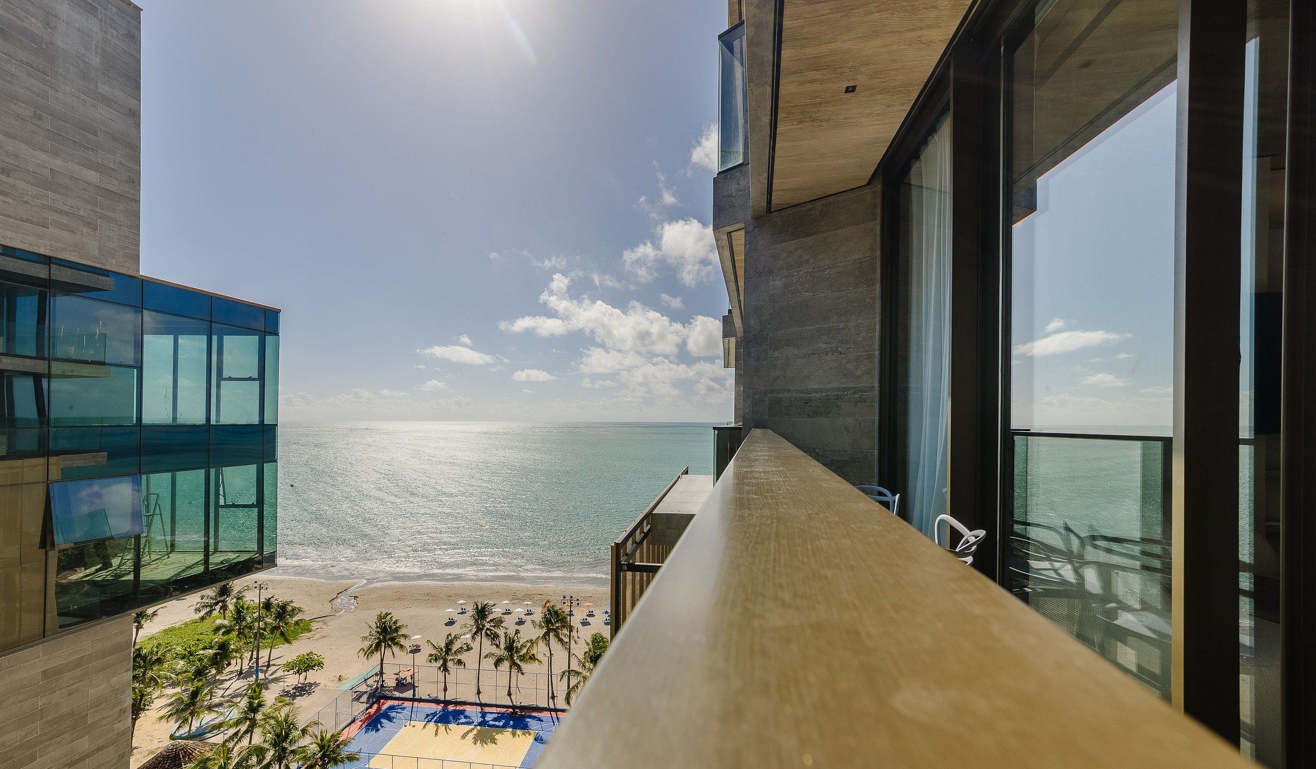 Un edificio moderno con grandes ventanales que dan a una playa y una zona de piscina.