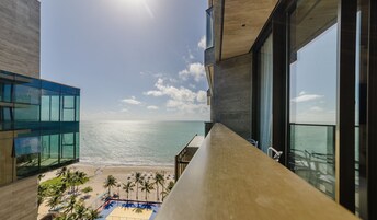A modern building with large windows overlooking a beach and a pool area.