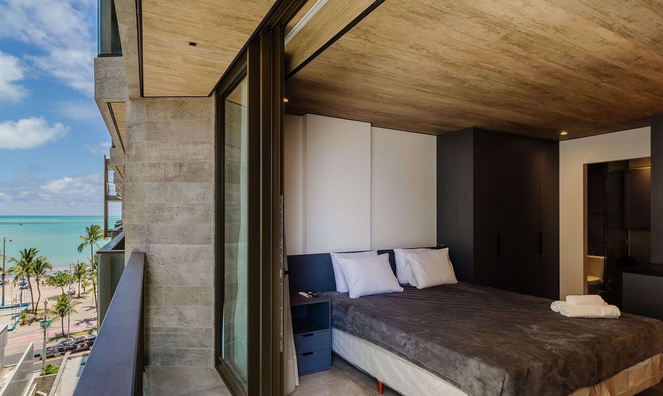 Un dormitorio moderno con una cama grande, una mesita de noche y vista a la playa.