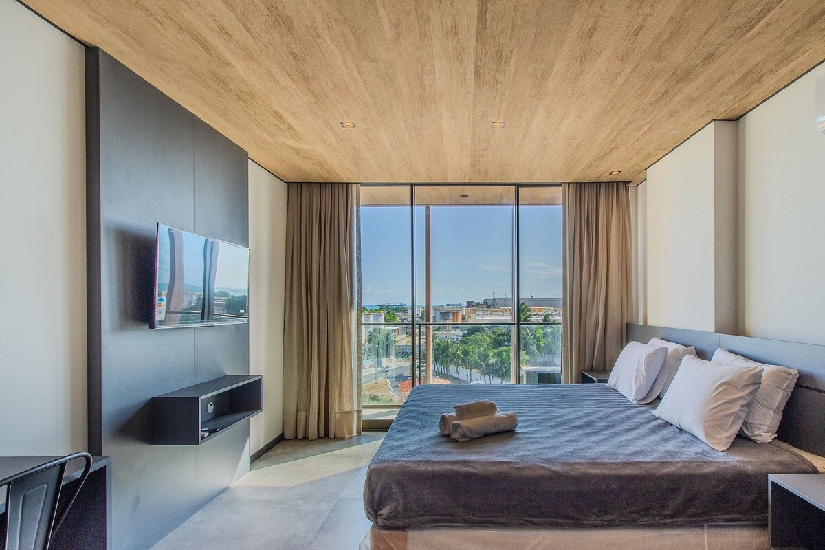 Ein modernes Hotelzimmer mit einem großen Bett, einem flachbildfernseher an der Wand und Blick auf die Stadt durch große Fenster.
