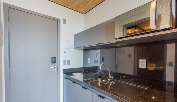 A modern kitchen with a black countertop, stainless steel sink, and a built-in oven. - NWTs - Estúdios com Vista Lateral Mar (Maceió)