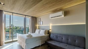 A modern bedroom with a large bed, a grey sofa, and a city view.