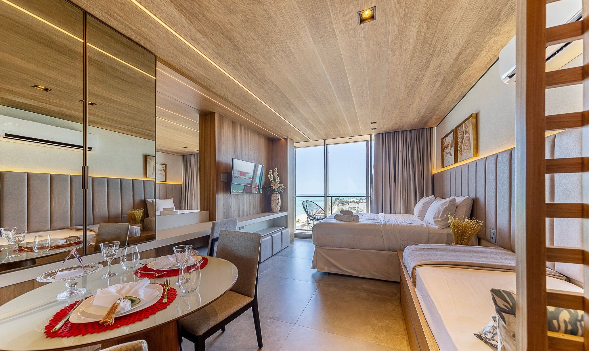 A modern hotel room with a dining area, a bed, and a large window offering a view.