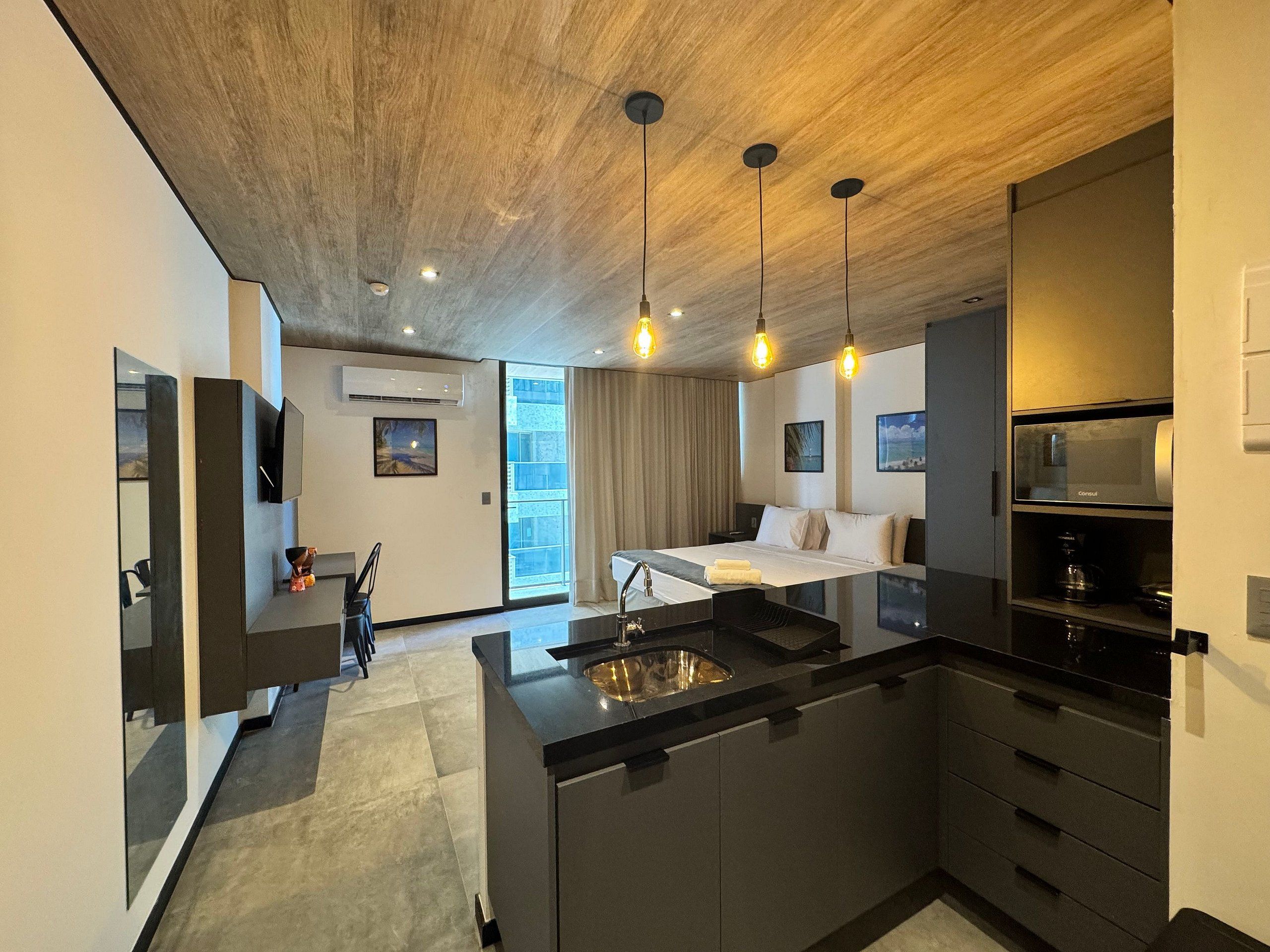 A modern hotel room with a large bed, a kitchen area with a sink, and a dining table.