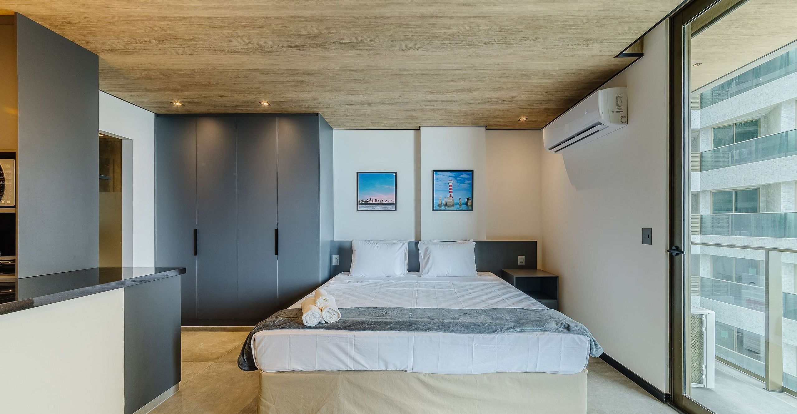 A modern hotel room with a bed, a wardrobe, a small bedside table, and a large window.