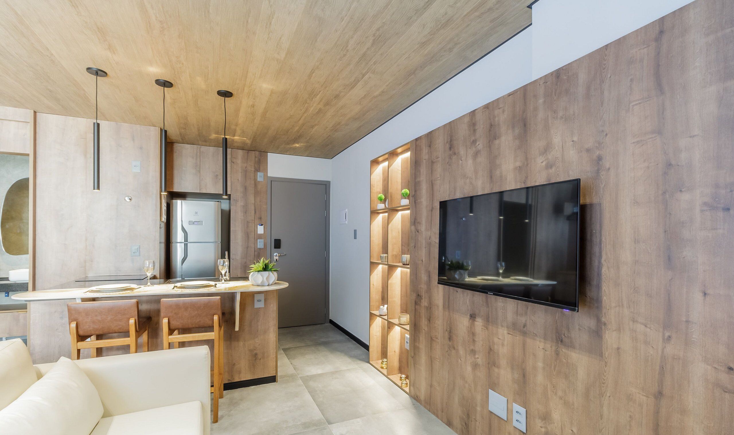 A modern kitchen with a built-in refrigerator, a dining area with a table and chairs, and a flat-screen TV mounted on the wall.