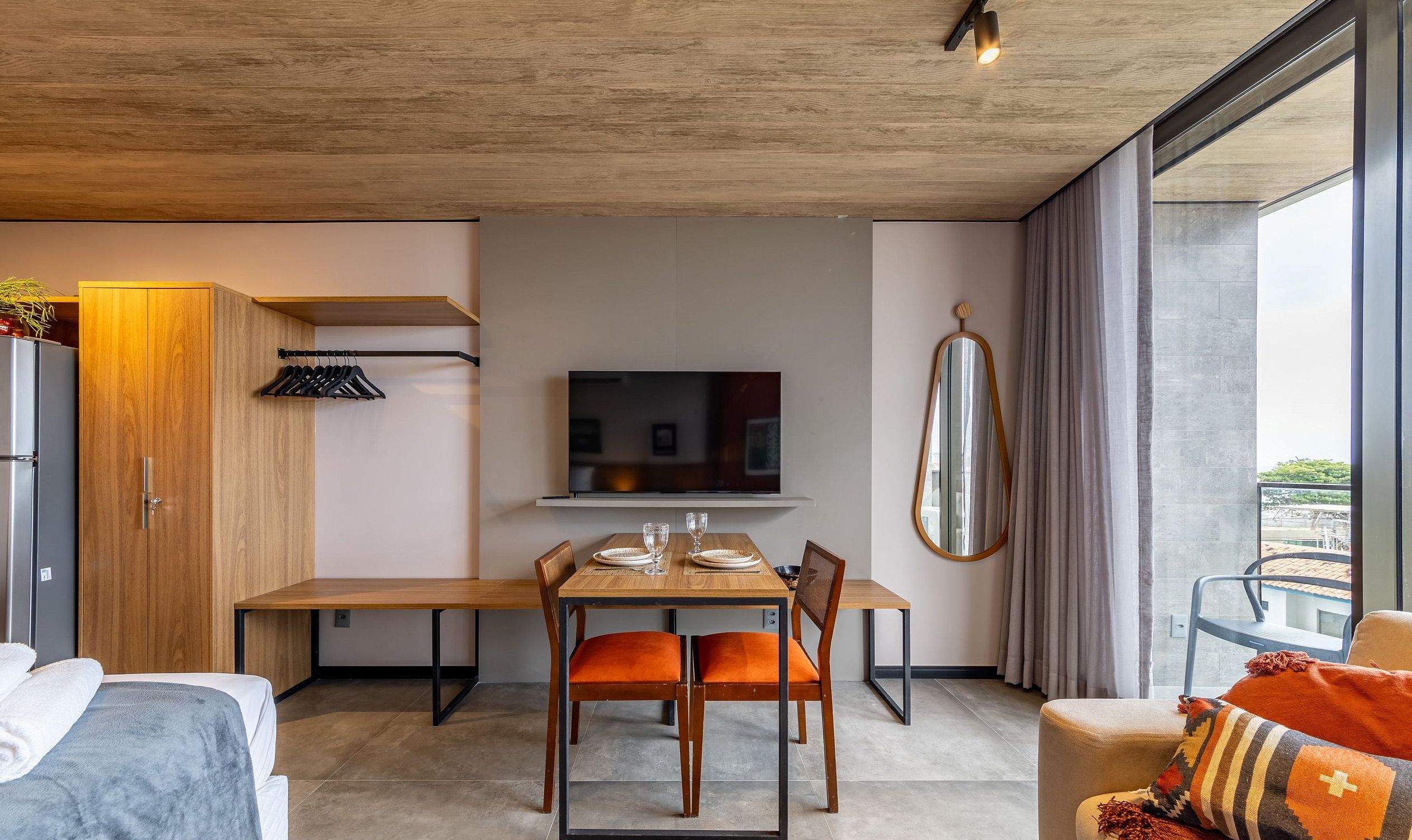 A modern hotel room with a dining area, a TV mounted on the wall, and a large window offering a view.