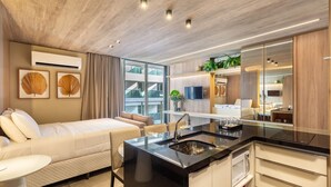A modern hotel room with a bed, a sitting area, a kitchen with a sink, and a large mirror. - NWTs - Estúdios com Vista Lateral Mar (Maceió)