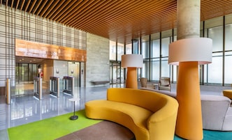 A modern lobby with a curved yellow sofa, a green carpet, and a wooden ceiling.