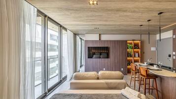 Una habitación de hotel moderna con un ventanal grande, un sofá, una zona de comedor y un televisor.