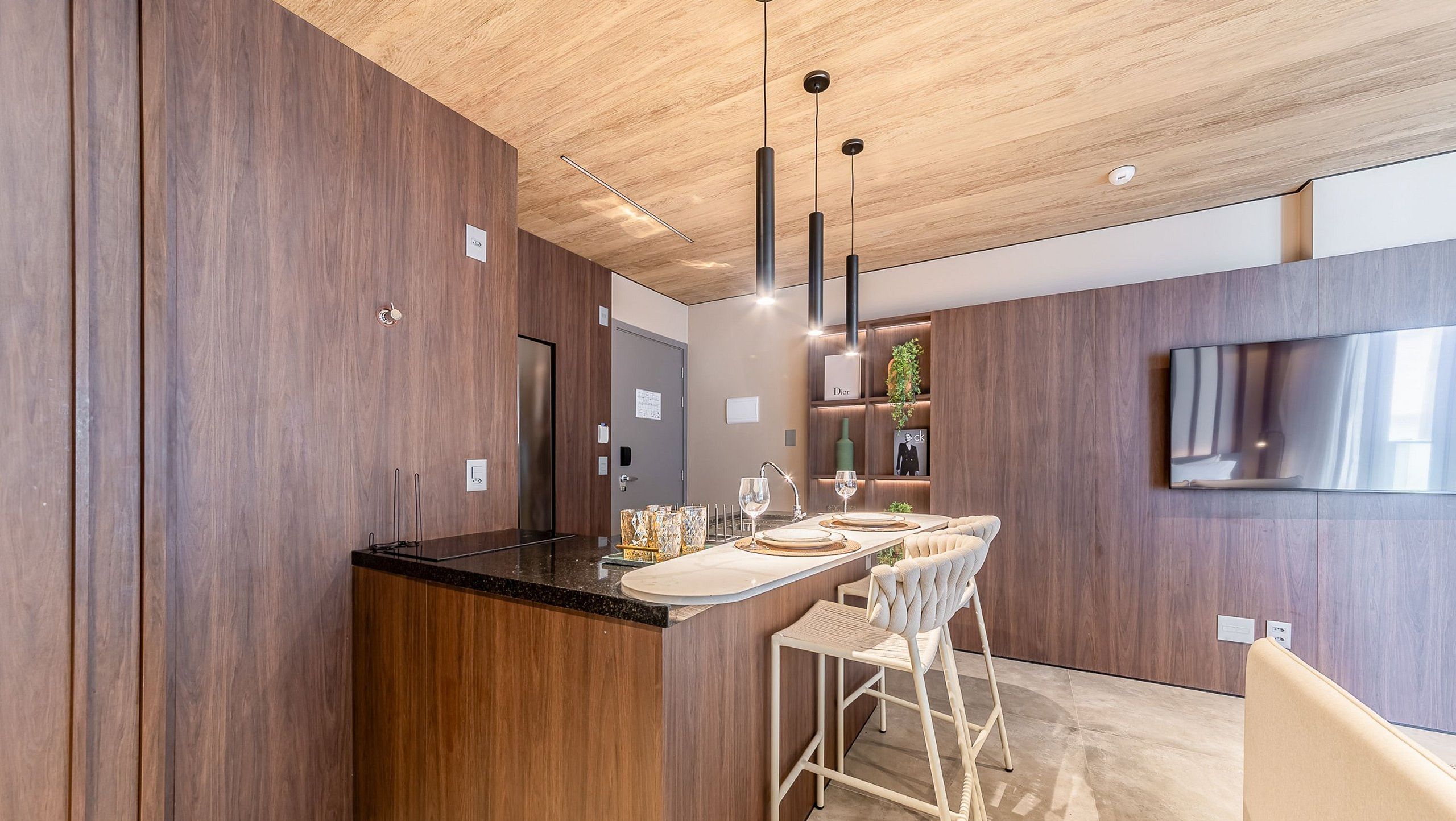 Een moderne keuken met een houten plafond, een geïntegreerd kookeiland met barkrukken, en een flatscreen televisie aan de muur.