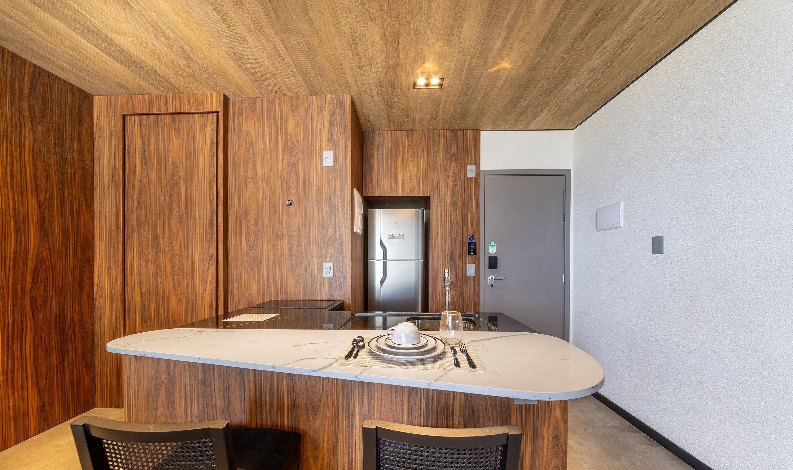 Una cocina moderna con una isla central, paneles de madera en las paredes y un refrigerador de acero inoxidable.