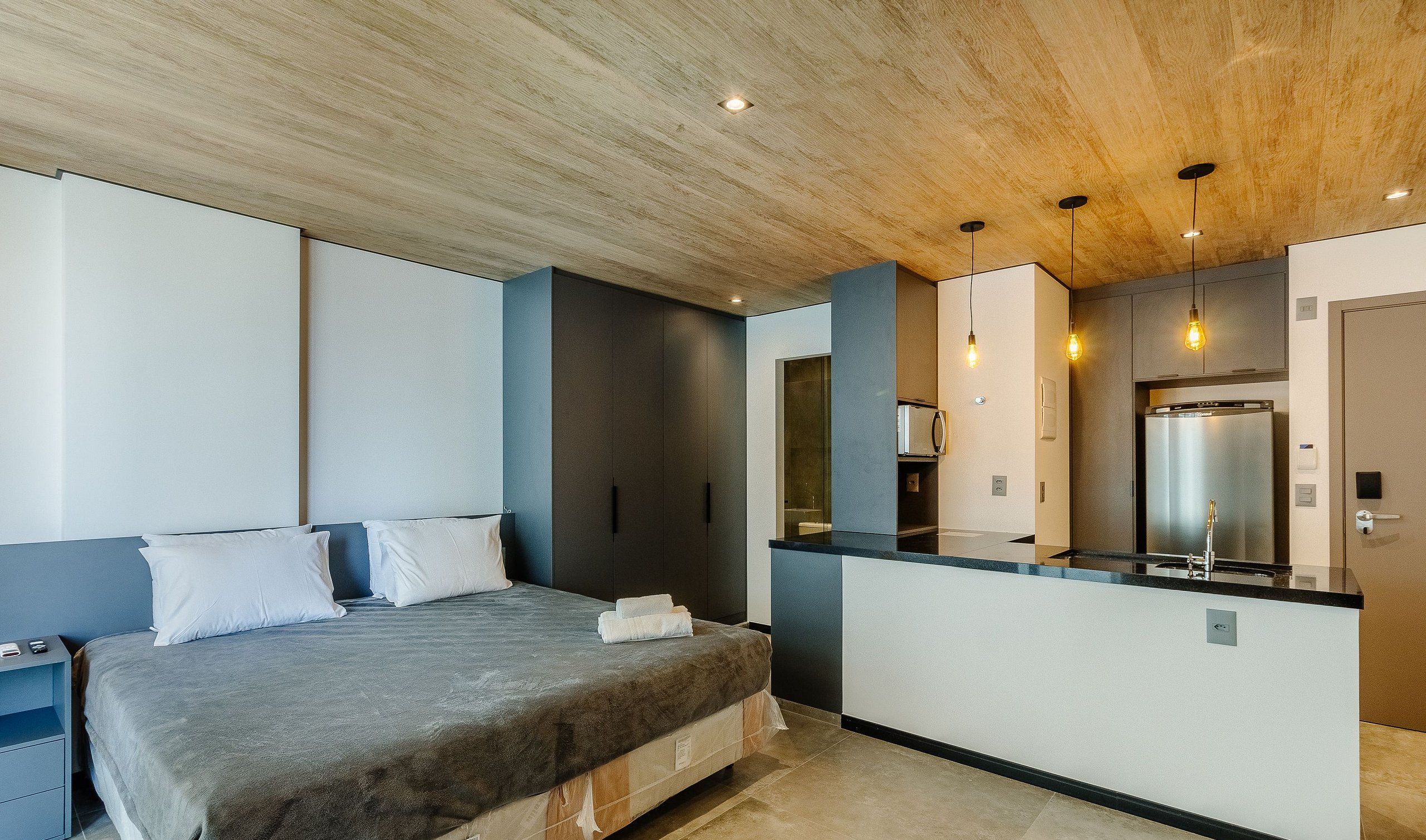 A modern bedroom with a large bed, a built-in wardrobe, and a kitchenette area.