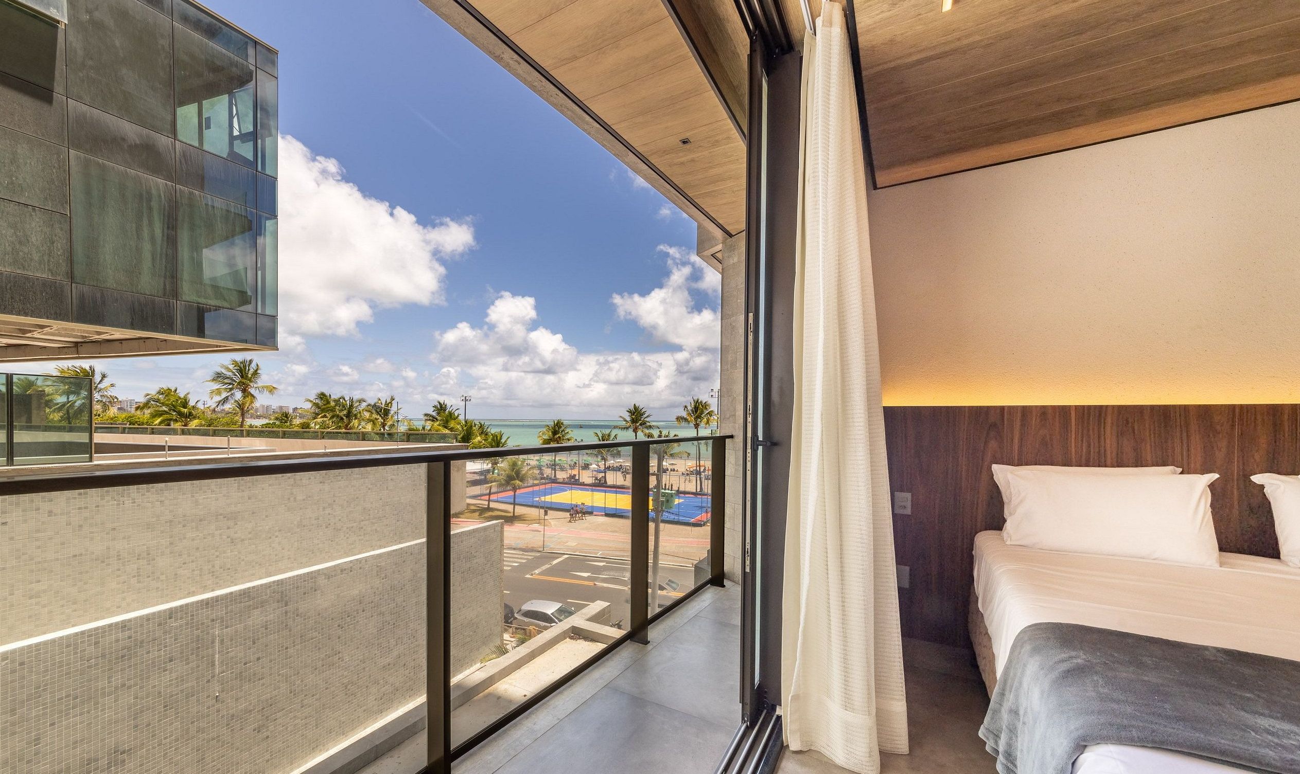 Habitación de hotel con balcón que da a una playa y al paisaje urbano.