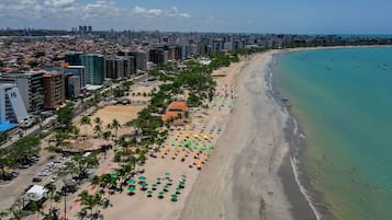 Paisagem costeira urbana com uma praia repleta de guarda-sóis e palmeiras.