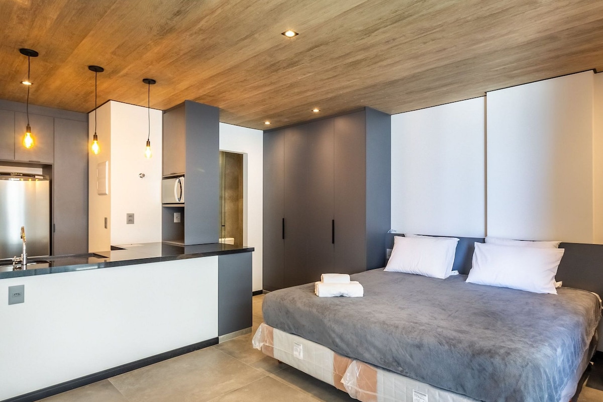 Un dormitorio moderno con una cama grande, mesitas de noche, un armario empotrado y una zona de cocina con un refrigerador.