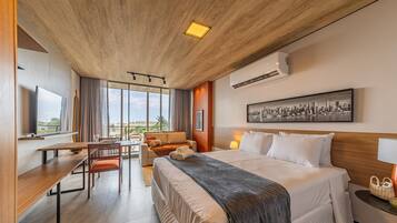 Hotelkamer met een bed, bureau, stoel, bank, raam met uitzicht, airconditioning en een kunstwerk aan de muur.